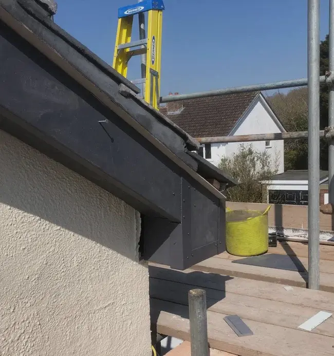 Completed dark roof-edge detail beside access scaffolding